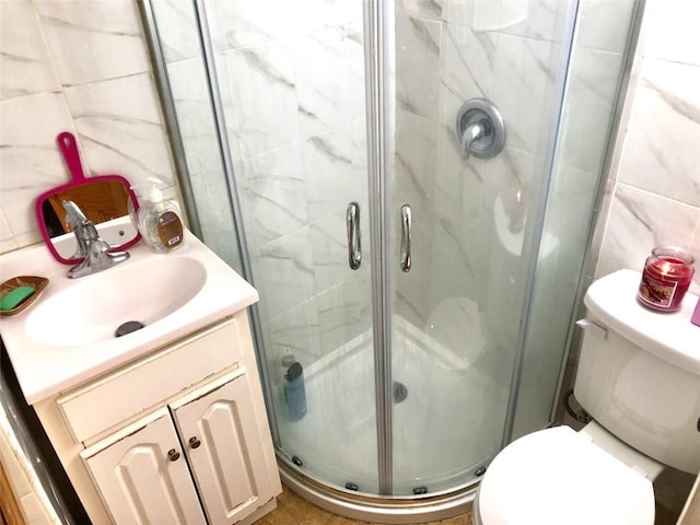 bathroom featuring a shower with shower door, tile walls, toilet, and vanity