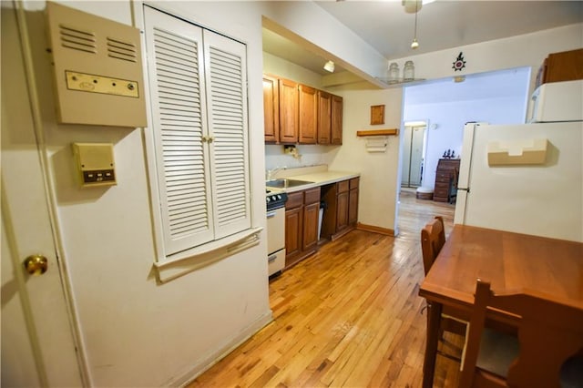 kitchen featuring light wood finished floors, light countertops, brown cabinetry, a sink, and white appliances