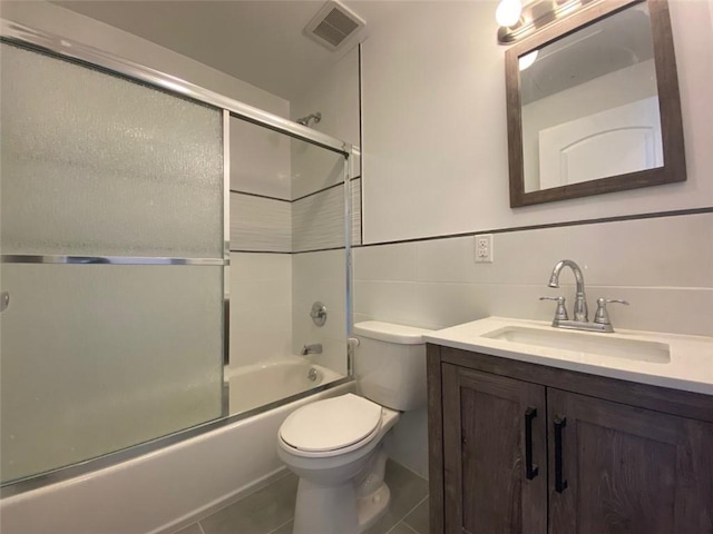 full bathroom featuring tile patterned floors, toilet, shower / bath combination with glass door, tile walls, and vanity