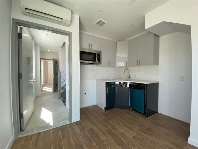 kitchen with gray cabinetry, a wall unit AC, black dishwasher, dark wood-type flooring, and tasteful backsplash