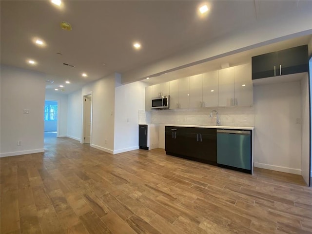 kitchen featuring appliances with stainless steel finishes, white cabinetry, decorative backsplash, and light hardwood / wood-style floors