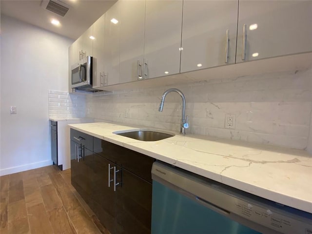 kitchen featuring dishwasher, sink, decorative backsplash, white cabinetry, and light stone counters