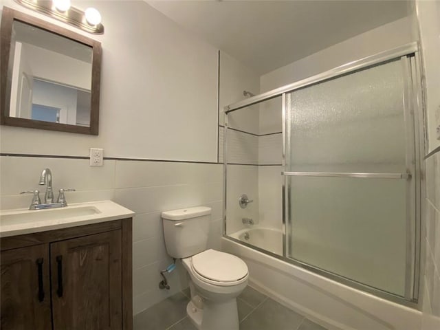 full bathroom with toilet, tile patterned floors, vanity, bath / shower combo with glass door, and tile walls