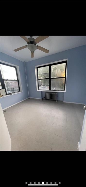 unfurnished room featuring baseboards, a ceiling fan, and radiator