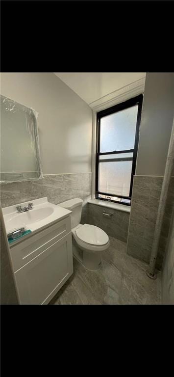 bathroom with wainscoting, tile walls, toilet, and vanity