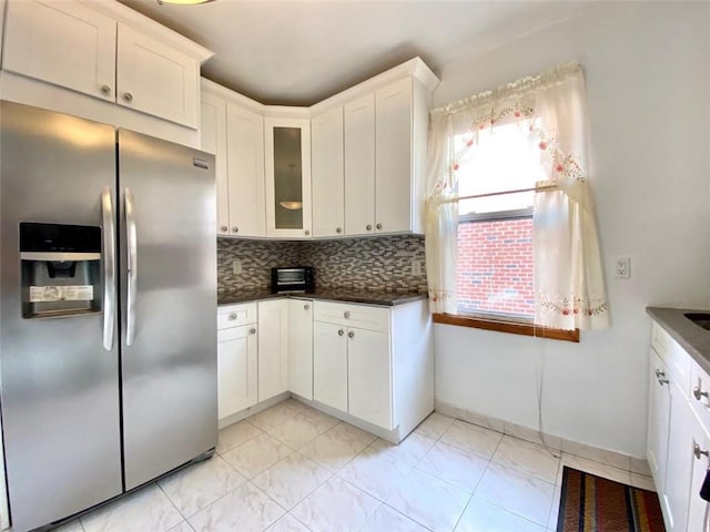 kitchen with white cabinets, stainless steel fridge, decorative backsplash, and dark stone countertops