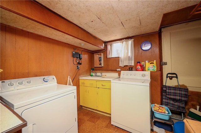 washroom featuring washing machine and dryer, a sink, wooden walls, and light floors