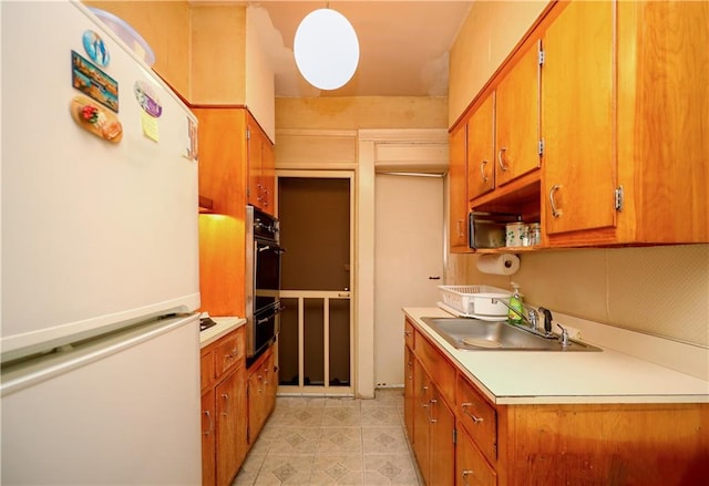 kitchen featuring brown cabinets, freestanding refrigerator, light countertops, pendant lighting, and a sink