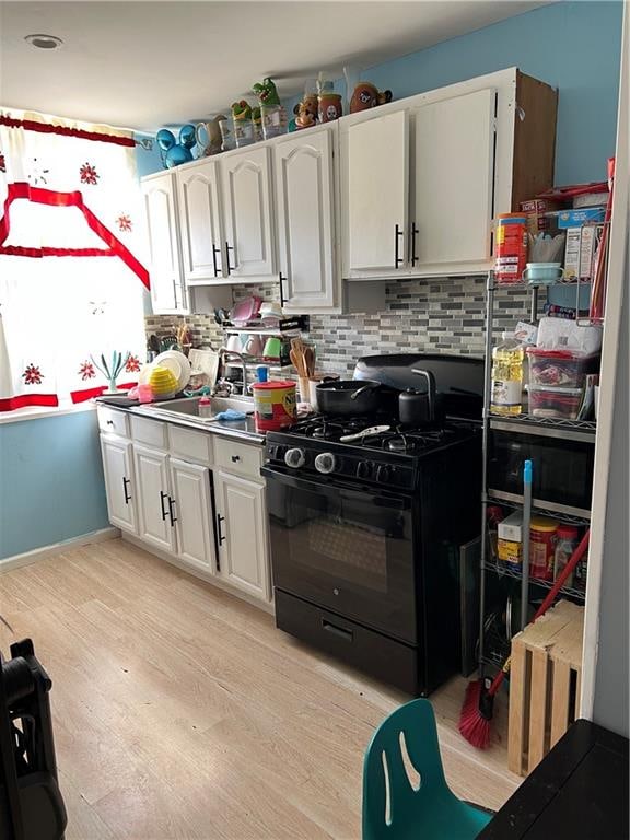 kitchen featuring black gas range, light wood-type flooring, white cabinetry, and backsplash