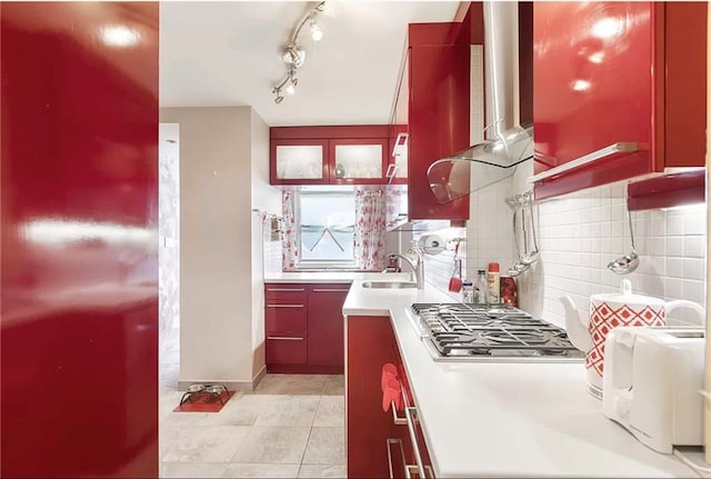 kitchen featuring stainless steel gas stovetop, backsplash, exhaust hood, sink, and light tile patterned floors