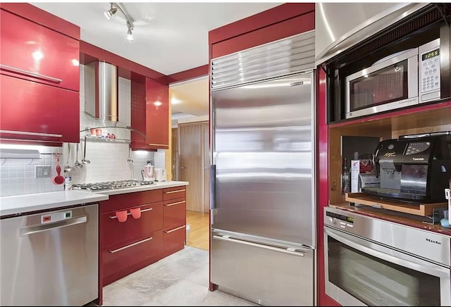 kitchen featuring built in appliances, wall chimney exhaust hood, light tile patterned floors, and tasteful backsplash