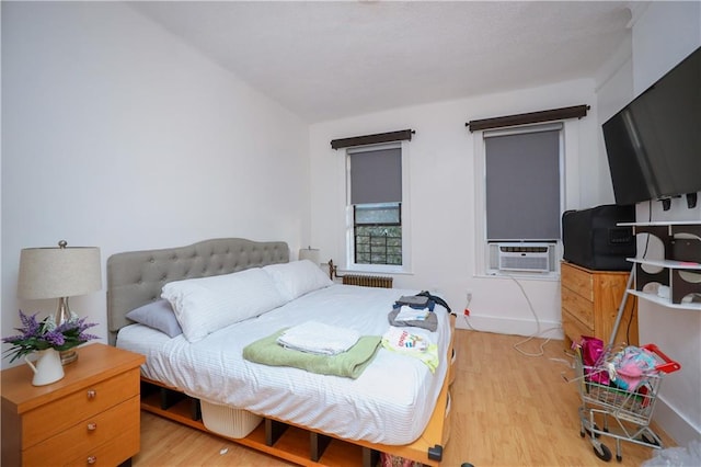 bedroom featuring radiator heating unit, cooling unit, and light hardwood / wood-style floors