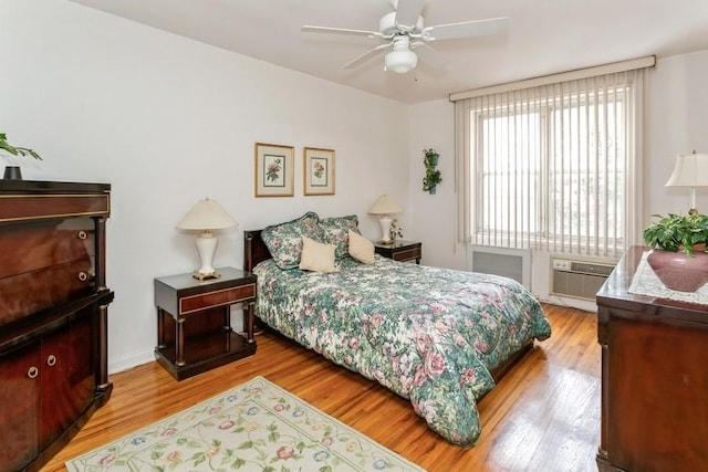 bedroom with ceiling fan, a wall unit AC, and light hardwood / wood-style flooring