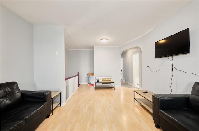 living area featuring ornamental molding, arched walkways, light wood-style flooring, and baseboards