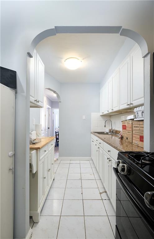 kitchen with light tile patterned floors, black gas stove, wood counters, and white cabinetry