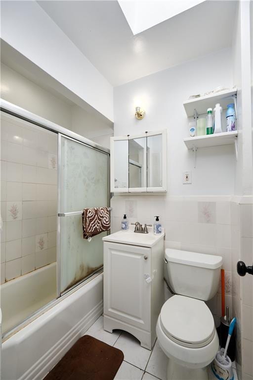 bathroom featuring a skylight, toilet, tile patterned floors, combined bath / shower with glass door, and tile walls