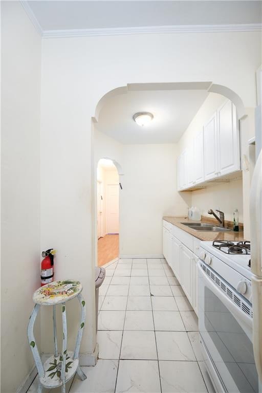 kitchen with arched walkways, ornamental molding, white cabinetry, white range with gas cooktop, and a sink