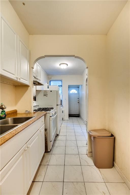 kitchen with arched walkways, a sink, white cabinetry, and white range with gas cooktop