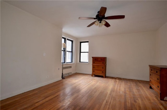 spare room featuring baseboards, ceiling fan, radiator heating unit, and light wood-style floors