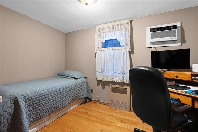 bedroom featuring light wood-type flooring, radiator, and a wall unit AC