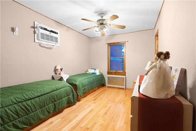 bedroom with radiator, ceiling fan, wood finished floors, and a wall mounted air conditioner