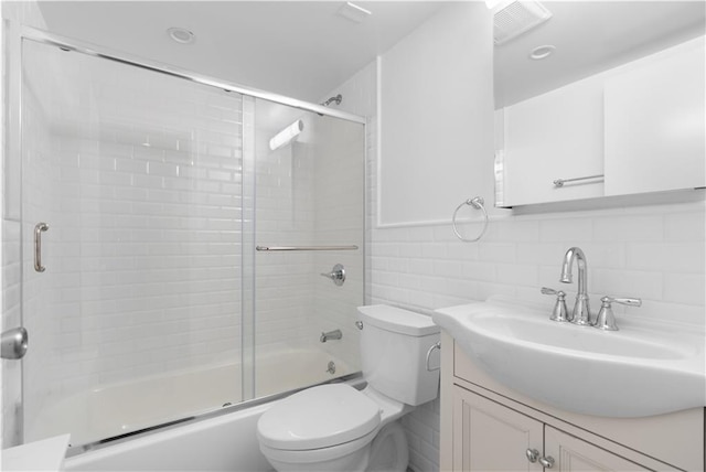 bathroom featuring visible vents, toilet, shower / bath combination with glass door, vanity, and tile walls