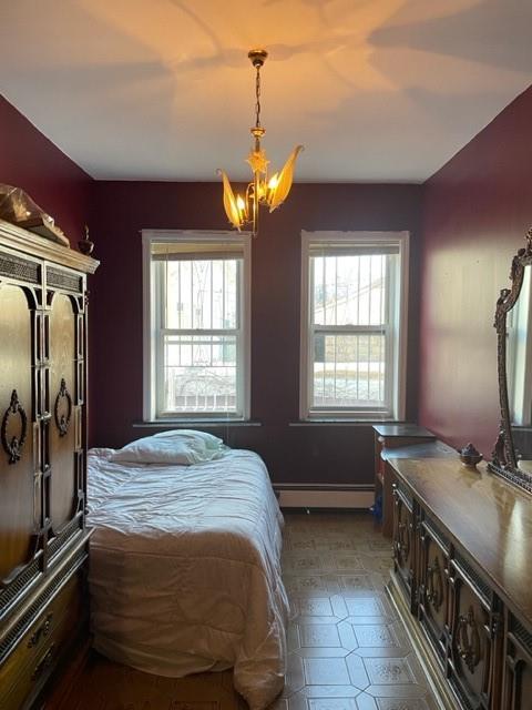 bedroom with an inviting chandelier, a baseboard radiator, and multiple windows