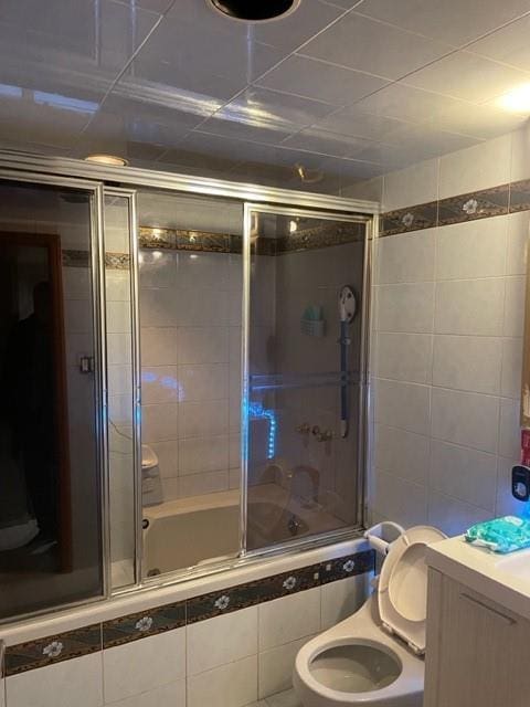 full bathroom featuring toilet, vanity, bath / shower combo with glass door, and tile walls