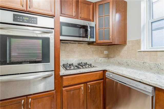 kitchen with light stone counters, brown cabinets, a warming drawer, appliances with stainless steel finishes, and glass insert cabinets