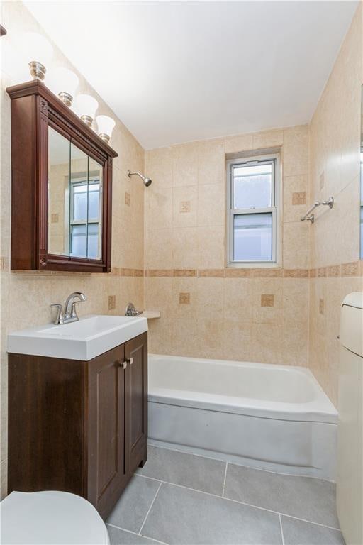 bathroom with toilet, tile patterned floors, vanity, shower / washtub combination, and tile walls