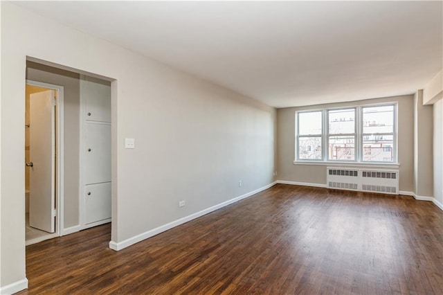 empty room featuring dark wood-style floors, baseboards, and radiator