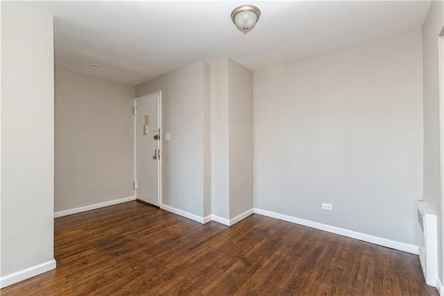 unfurnished room featuring dark wood-style floors, radiator heating unit, and baseboards