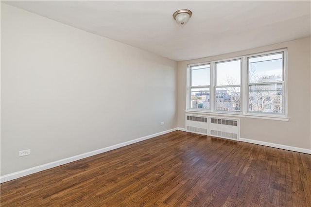 empty room with radiator heating unit, baseboards, and dark wood-type flooring