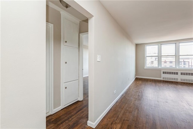 unfurnished room featuring dark wood-style floors, baseboards, and radiator heating unit