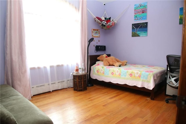 bedroom with wood-type flooring and a baseboard heating unit