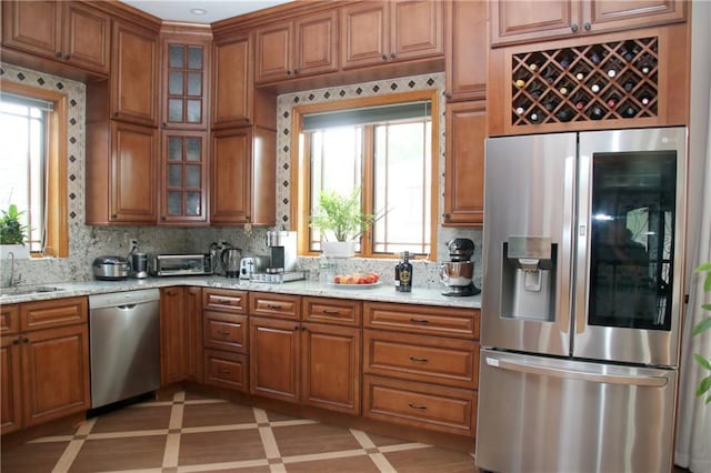 kitchen with light stone countertops, decorative backsplash, stainless steel appliances, and a wealth of natural light