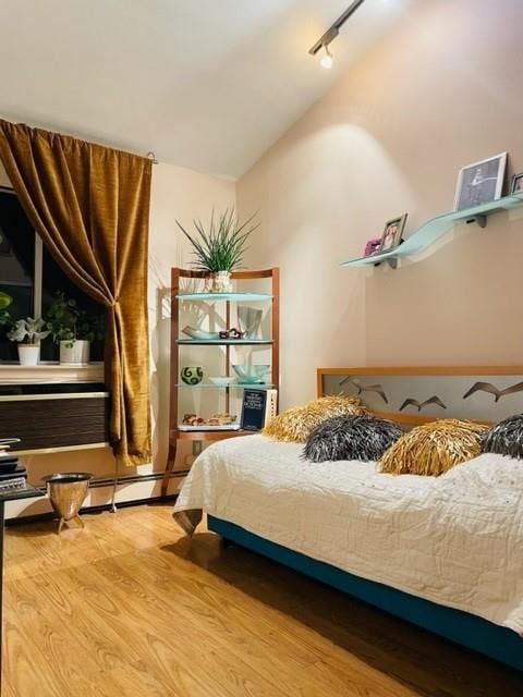 bedroom with track lighting, wood-type flooring, and a baseboard radiator