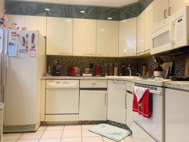 kitchen with tasteful backsplash, white cabinetry, light tile patterned floors, and white appliances