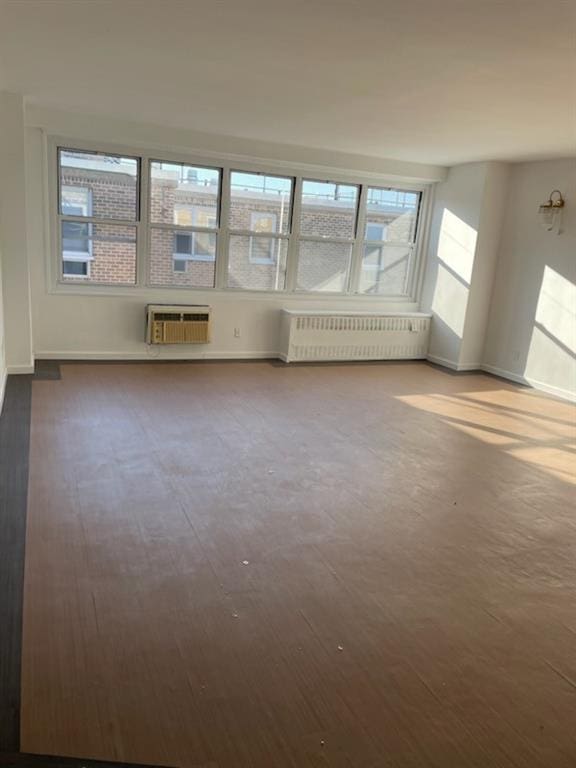 empty room with radiator, a wall unit AC, baseboards, and wood finished floors