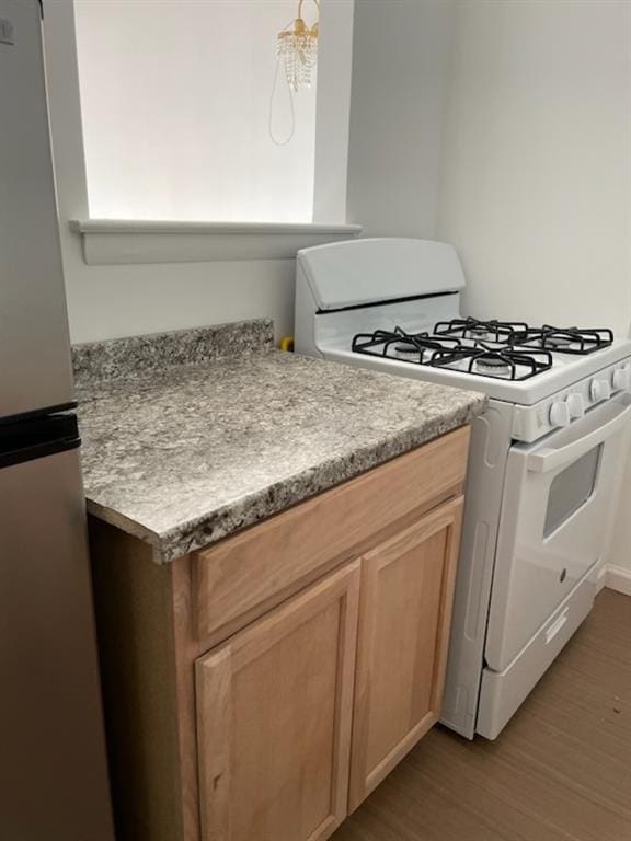 kitchen with light countertops, wood finished floors, freestanding refrigerator, and white range with gas stovetop