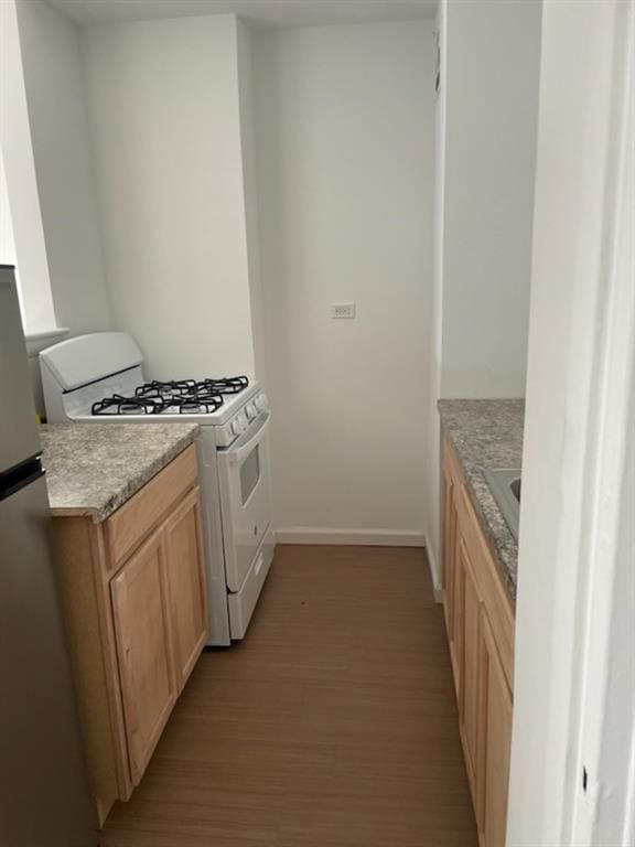 kitchen with baseboards, freestanding refrigerator, light countertops, light wood-style floors, and gas range gas stove