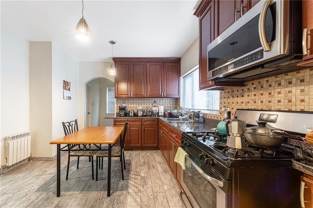 kitchen featuring appliances with stainless steel finishes, light wood-type flooring, tasteful backsplash, pendant lighting, and radiator heating unit