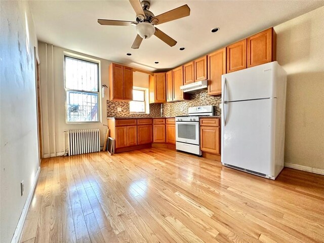 kitchen with light wood-type flooring, tasteful backsplash, radiator heating unit, stainless steel gas stove, and white fridge