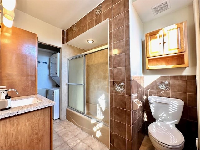 full bathroom with toilet, bath / shower combo with glass door, tile walls, and stacked washer and clothes dryer