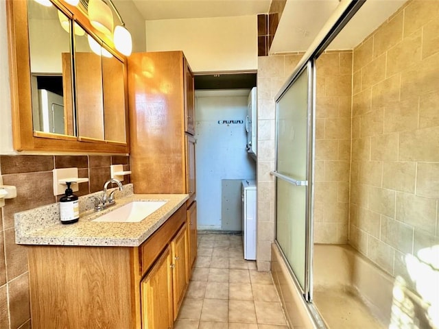 bathroom with tile patterned flooring, backsplash, combined bath / shower with glass door, vanity, and tile walls