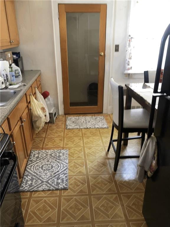 kitchen featuring a sink, brown cabinets, stove, and freestanding refrigerator