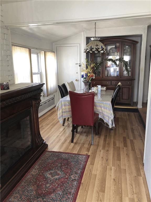 dining room with light wood finished floors, a glass covered fireplace, vaulted ceiling, and a baseboard radiator