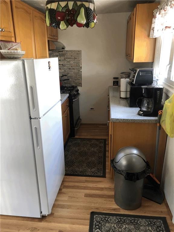 kitchen with black gas range, light wood-style flooring, brown cabinets, and freestanding refrigerator