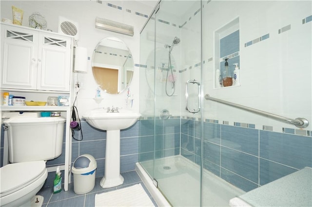 bathroom featuring toilet, tile patterned floors, tile walls, and a shower with shower door