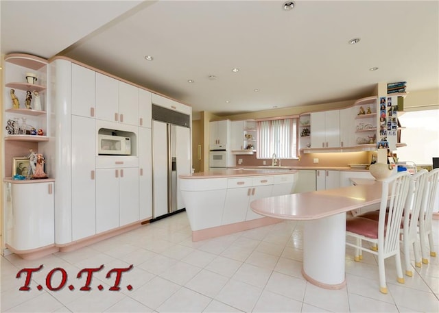 kitchen with light tile patterned floors, white appliances, a kitchen island, white cabinets, and sink